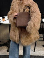 woman holding a brown handbag while wearing a shaggy brown faux fur coat and blue jeans