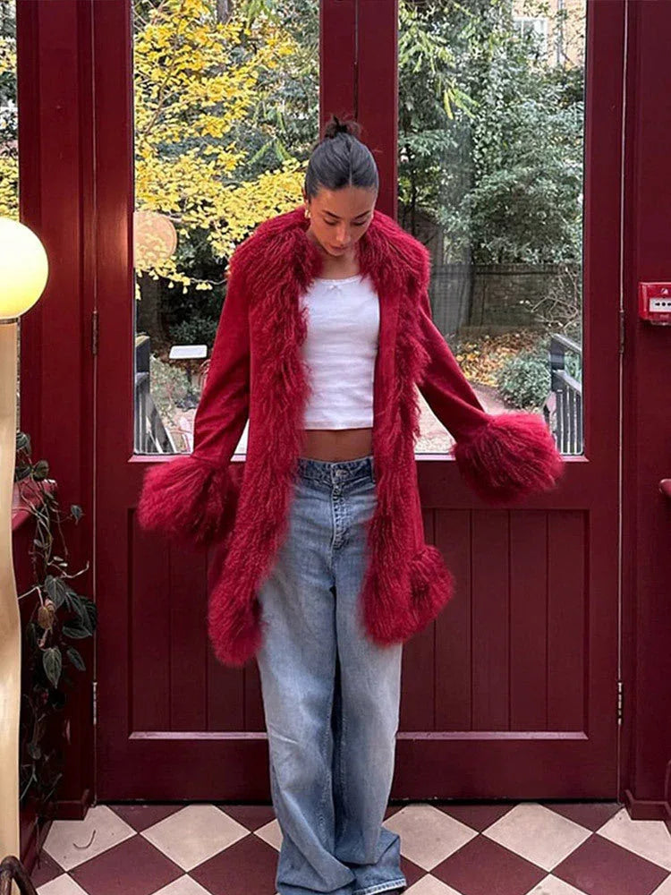 Woman wearing a red suede coat with fluffy red fur trim and cuffs, paired with a white crop top and blue jeans, standing in front of a red door. Main image