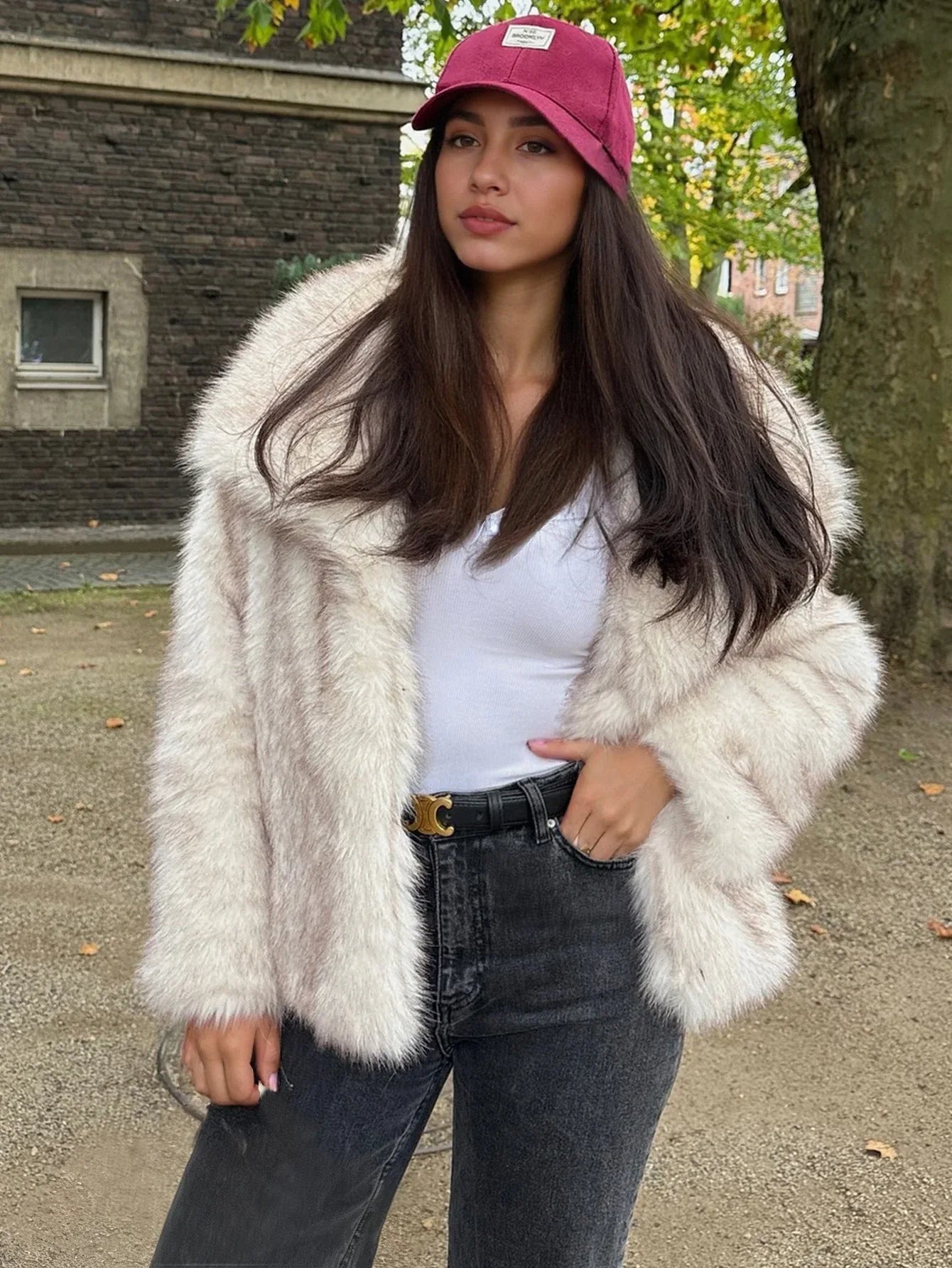 Woman in a cream faux fur jacket, white tank top, and dark jeans, outdoors.