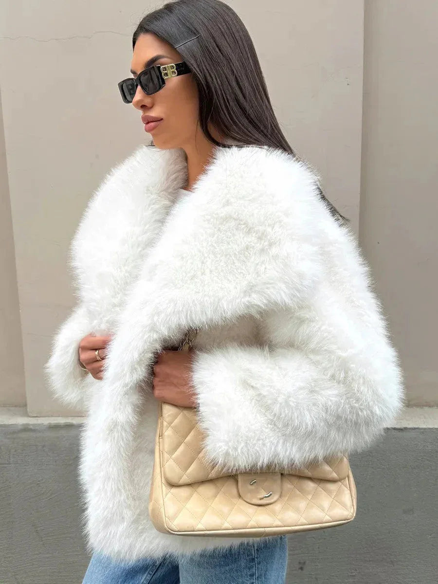 Woman wearing a white faux fur jacket with a large collar, blue jeans, and sunglasses, holding a beige quilted handbag.