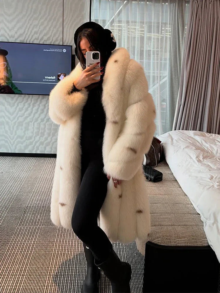 Woman wearing a long white faux fur coat with brown accents, black turtleneck, black leggings, and black boots, holding a phone to take a mirror selfie.