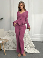 Woman standing in a pink ribbed knit loungewear set with flared sleeves and wide leg pants.
