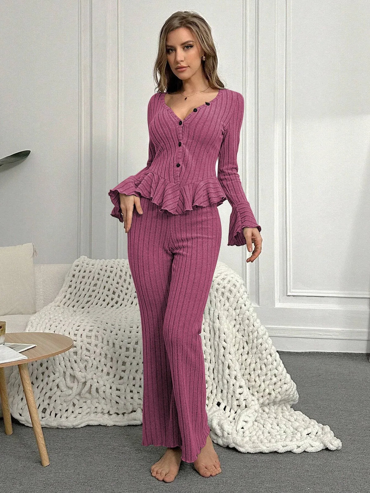 Woman standing in a pink ribbed knit loungewear set with flared sleeves and wide leg pants.