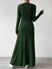 Back view of a woman wearing a long-sleeved green ribbed maxi dress, posing against a white wall.