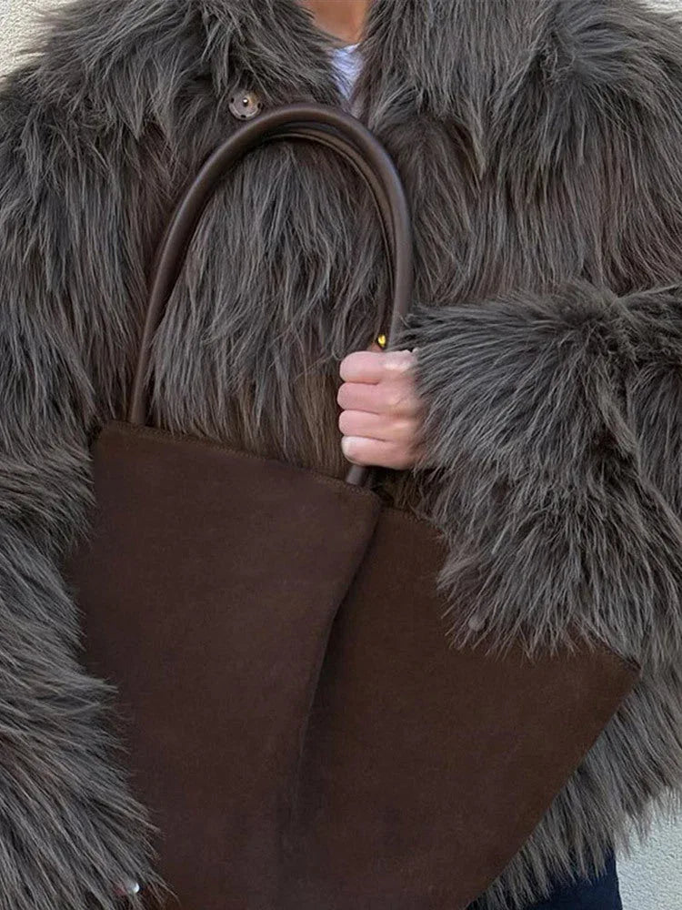 Close-up of a woman's hands holding a brown tote bag, with a shaggy grey faux fur jacket visible.