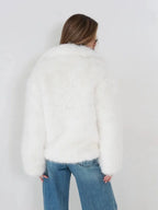 Back view of a woman wearing a white faux fur jacket and blue jeans.