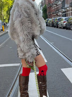 Woman wearing a faux fur jacket, leopard print skirt, and red socks while standing on a street.