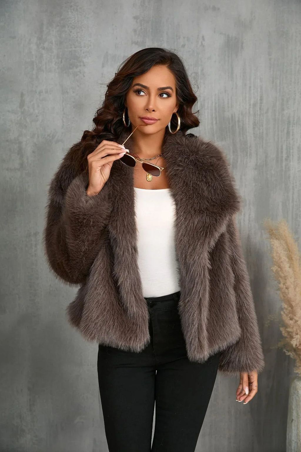 Woman wearing a brown faux fur jacket, white top, and black pants, looking to the side.