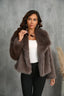 Woman wearing a brown faux fur jacket, white top, and black pants, looking to the side.