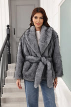 Woman wearing a grey faux fur jacket with a belt tied at the waist, paired with blue jeans.