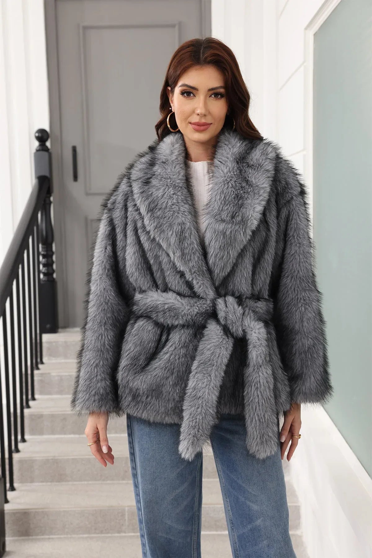 Woman wearing a grey faux fur jacket with a belt tied at the waist, paired with blue jeans.
