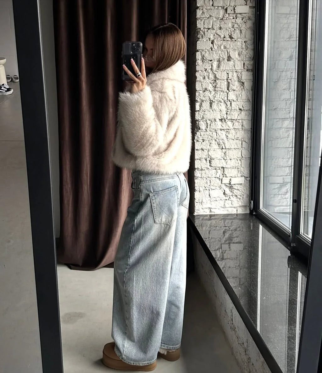 Full body mirror selfie of a woman in a cream faux fur cropped jacket and light wash wide-leg jeans.