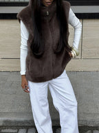 Front view of a woman wearing a brown faux fur vest, white long-sleeved shirt, and white pants.