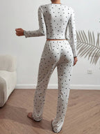 Rear view of a woman wearing a white long-sleeve pajama set with a black heart print, standing.