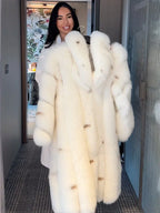 Woman holding a long white faux fur coat on a hanger, smiling.