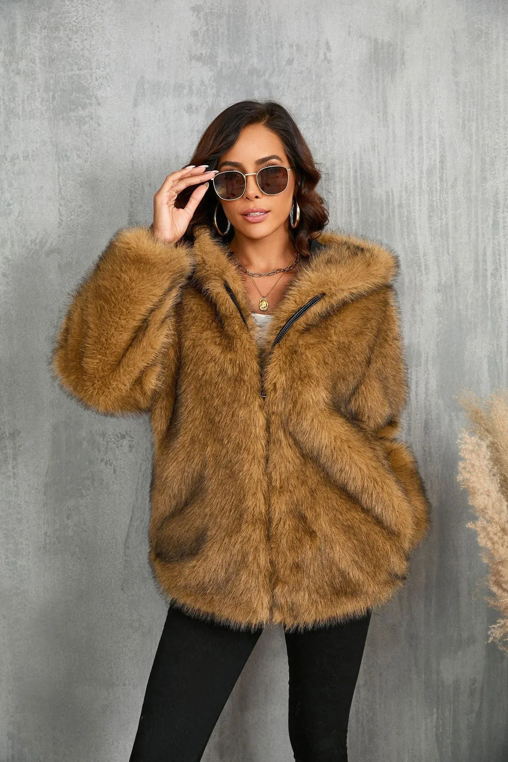 Woman wearing a brown faux fur hooded jacket, adjusting her sunglasses.