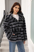 Woman wearing a hooded faux fur jacket with horizontal black and grey stripes and a belted waist.