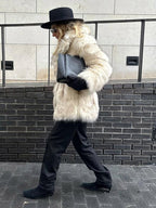 Side view of a woman in a cream faux fur coat, black hat, and black pants walking outdoors.