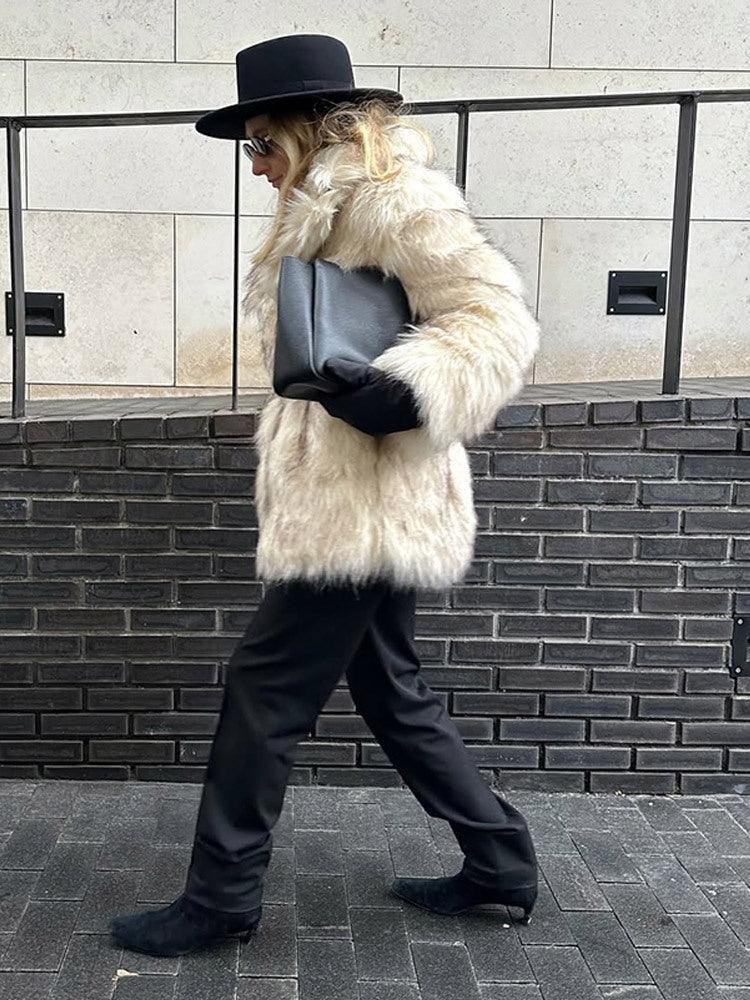Side view of a woman in a cream faux fur coat, black hat, and black pants walking outdoors.
