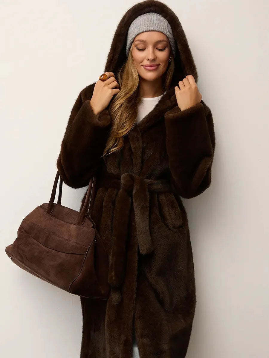 Woman in a brown hooded faux fur coat, grey beanie, and holding a brown suede bag.