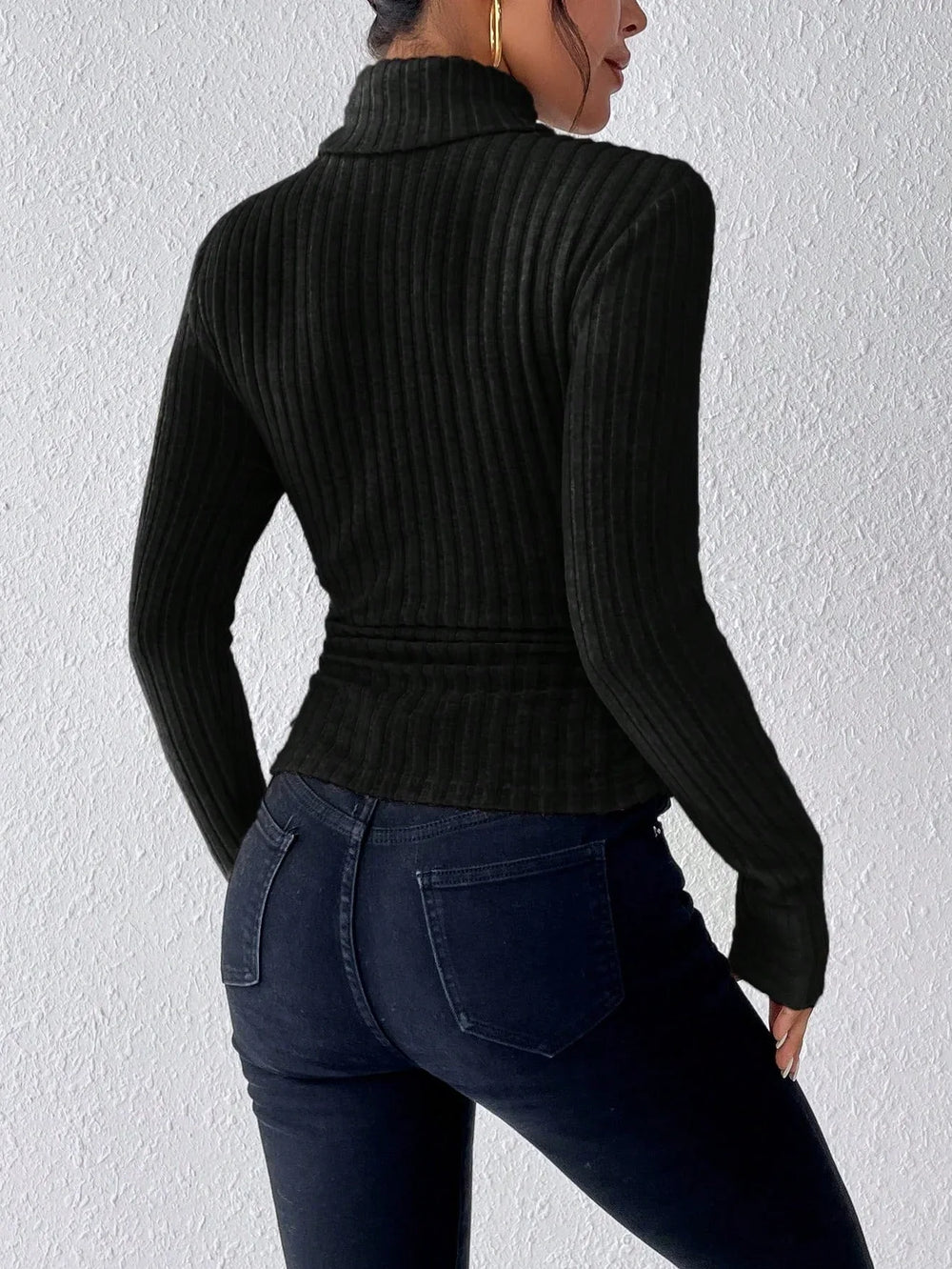 Back view of a woman wearing a black ribbed turtleneck sweater and dark wash jeans.