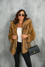 Woman wearing a brown faux fur hooded jacket with a white top, black pants, and a black quilted handbag.