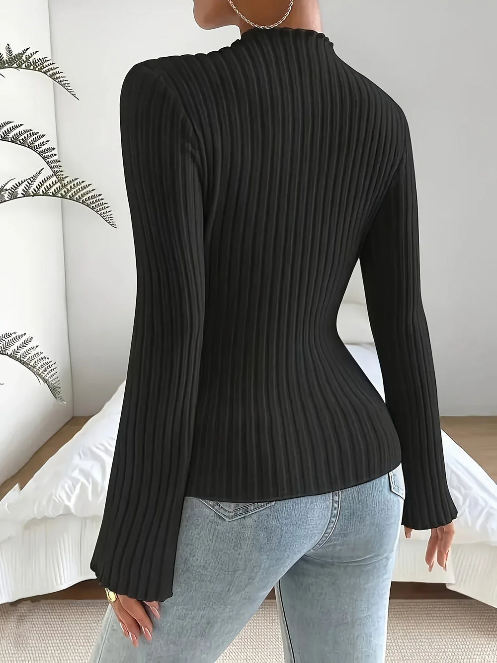 Back view of a woman wearing a black ribbed long-sleeve top with flared sleeves and light-wash denim jeans.