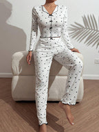 Woman wearing a white long-sleeve pajama set with a black heart print, sitting on a white armchair with one leg extended.