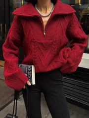 Woman wearing a red textured knit quarter zip sweater and black pants, holding a book and a handbag.