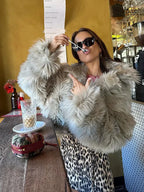 Woman posing in a faux fur jacket and leopard print skirt at a cafe.