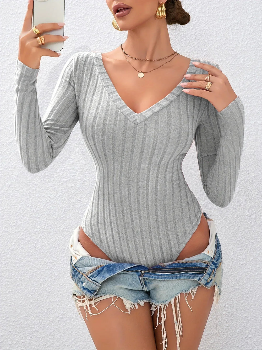 Model wearing a grey ribbed long-sleeve bodysuit with denim shorts and jewelry.