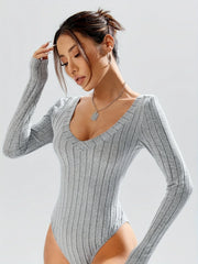 Close-up of a woman wearing a grey ribbed long-sleeve bodysuit, touching her hair.