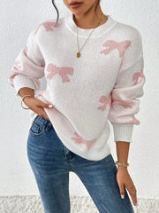 Woman wearing a white crew neck sweater with pink bow print and blue jeans, holding her hand on her hip