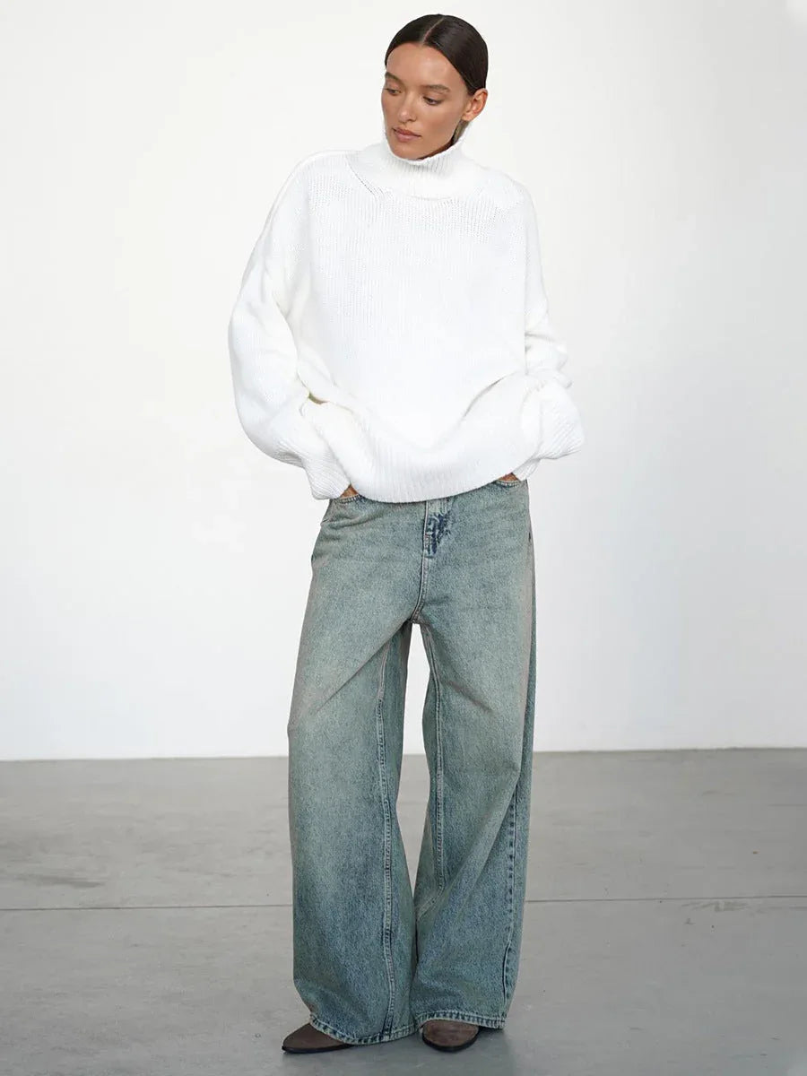 Woman wearing an oversized white turtleneck sweater with wide-leg blue jeans, hands in pockets.