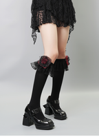 Detail of black knee-high socks with black lace ruffles and red rose accents worn with black platform shoes.