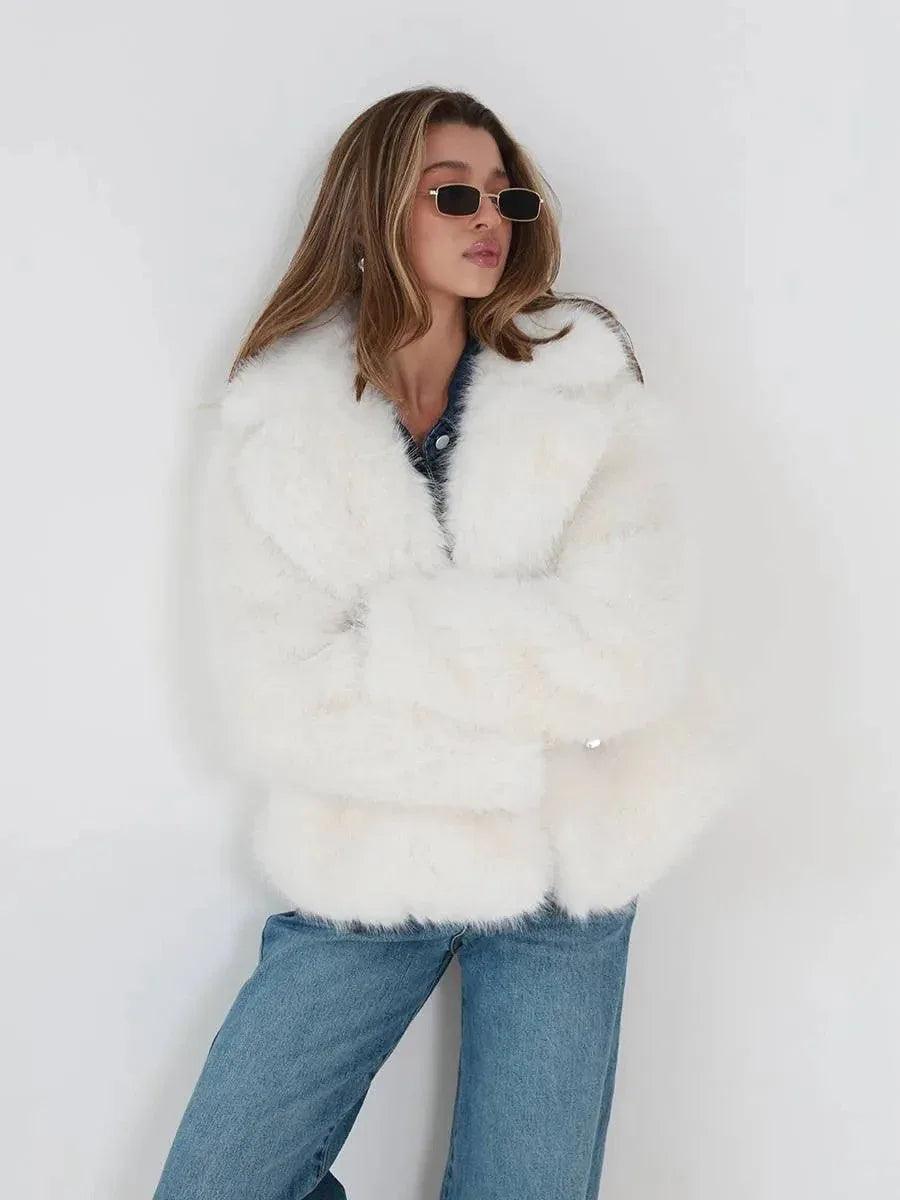 Woman wearing a white faux fur jacket over a denim shirt and blue jeans, leaning against a white wall. Main image