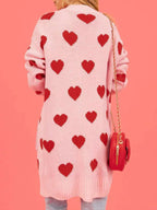 Back view of a woman wearing a pink longline cardigan with a repeating red heart pattern.