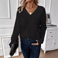 Woman in a black ribbed V-neck long-sleeve sweater and dark wash jeans, holding a black handbag with a chain strap.