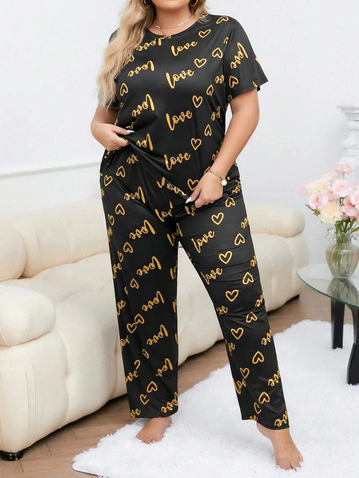 Woman wearing a black and gold "love" and heart print pajama set standing. Main image