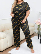 Woman wearing a black and gold "love" and heart print pajama set standing.