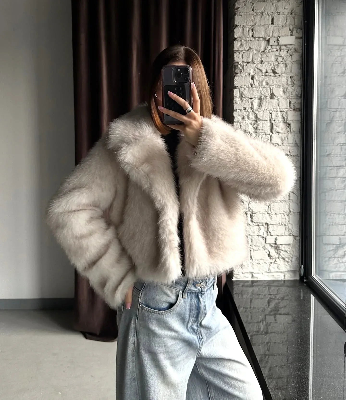 Woman wearing a cream faux fur cropped jacket and light wash wide-leg jeans, holding a phone to take a mirror selfie. Main image
