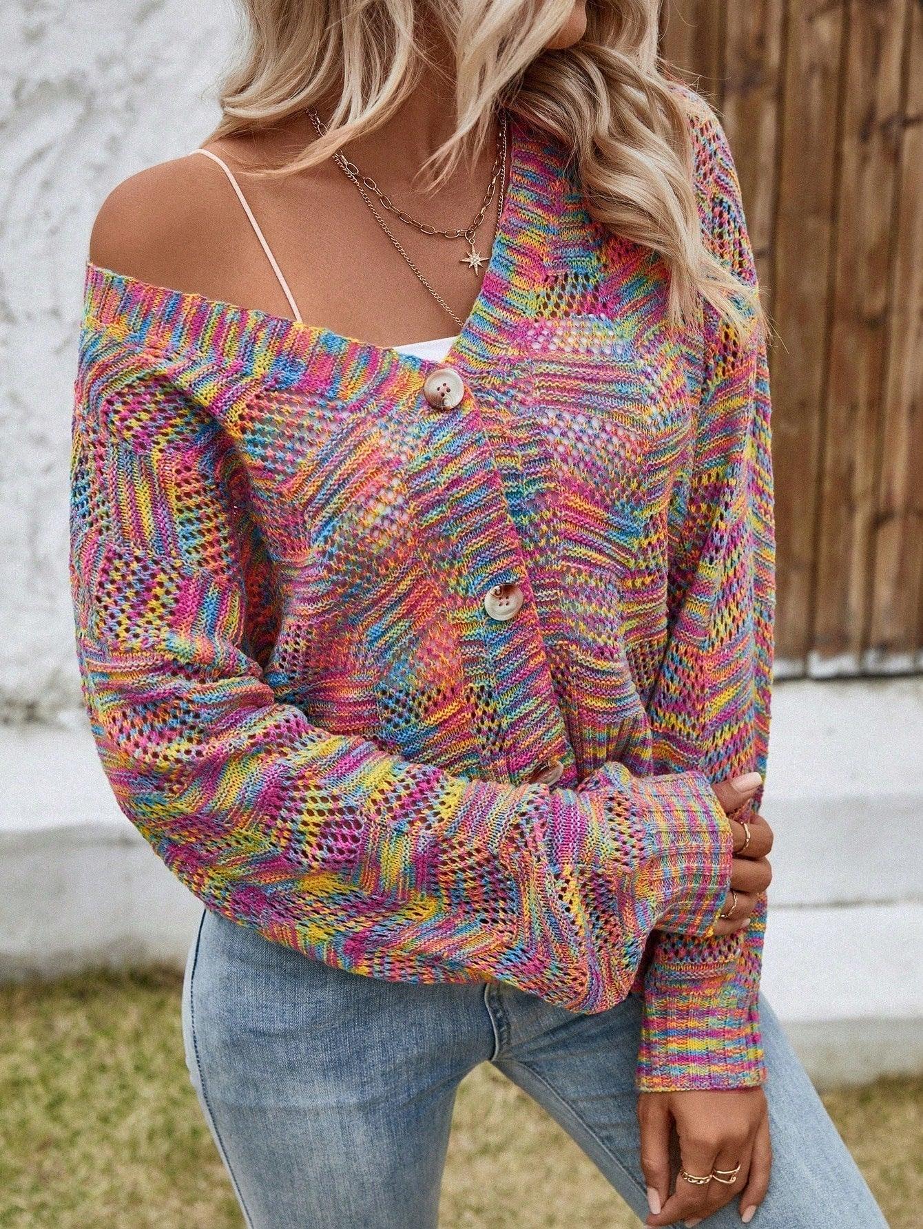 Woman wearing a multicolor rainbow knit cropped cardigan, white top, and blue jeans, with one shoulder strap visible.