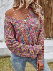 Woman wearing a multicolor rainbow knit cropped cardigan, white top, and blue jeans, with one shoulder strap visible.