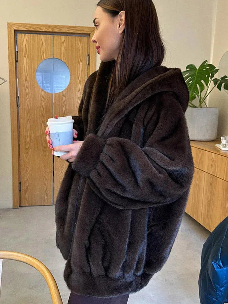 Close-up of a woman wearing a brown faux fur hooded jacket indoors, holding a coffee cup.