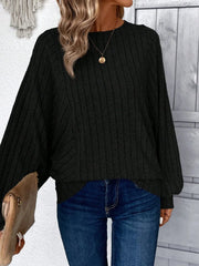 Woman wearing a black ribbed knit sweater with batwing sleeves and blue jeans, holding a tan clutch.