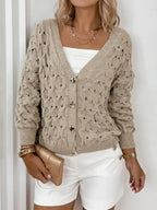 Woman's torso showing a beige open-knit V-neck cardigan with gold buttons, a white tube top, and white shorts.