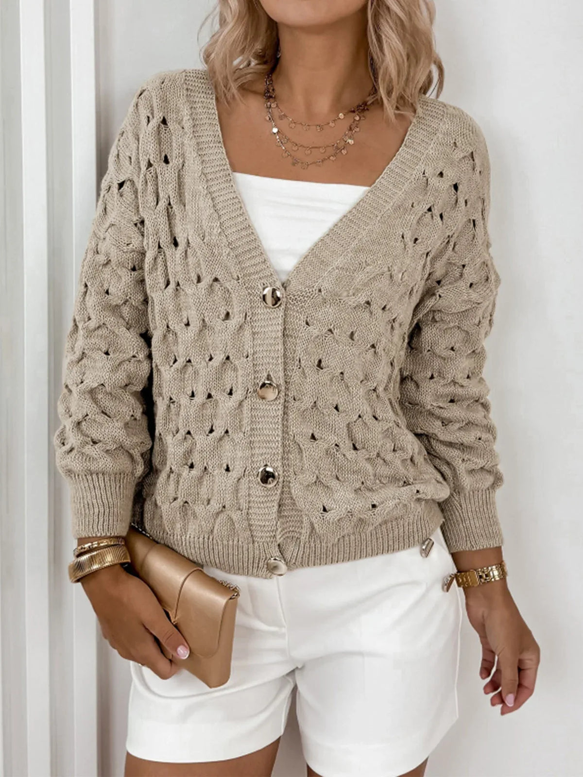 Woman's torso showing a beige open-knit V-neck cardigan with gold buttons, a white tube top, and white shorts.