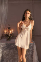 Woman wearing a white satin babydoll nightgown with lace trim and a matching robe, leaning on a table with candles.