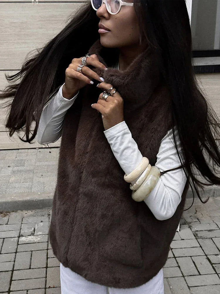 Close-up of a woman adjusting the collar of her brown faux fur vest, showcasing jewelry.