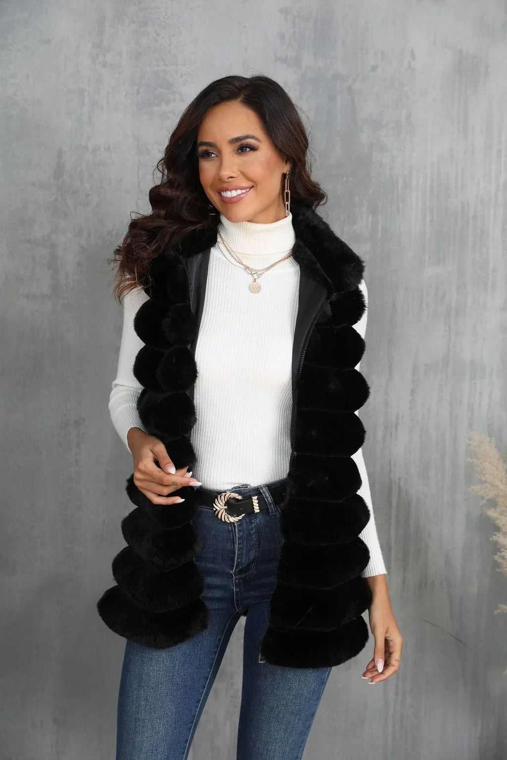 Woman wearing a black faux fur vest over a white turtleneck and blue jeans, looking to the side.